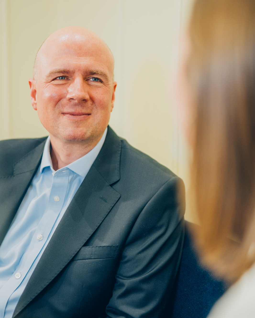 Arzt im Anzug im Gespräch mit einer Patientin in einem Behandlungsraum.