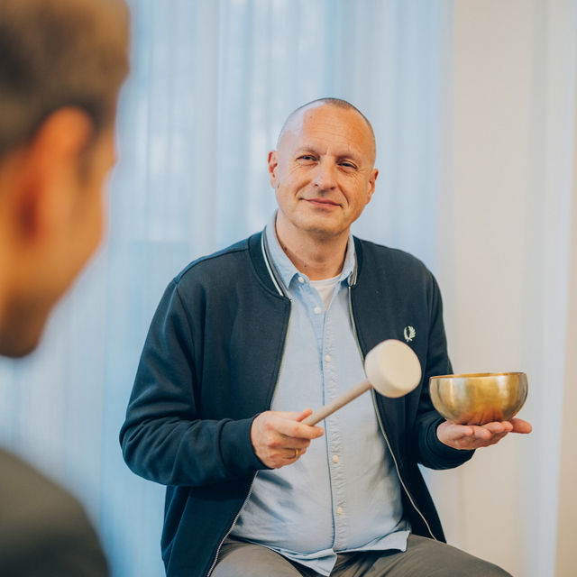 Co-Therapeut hält eine Klangschale während eines Gesprächs mit einer Person.