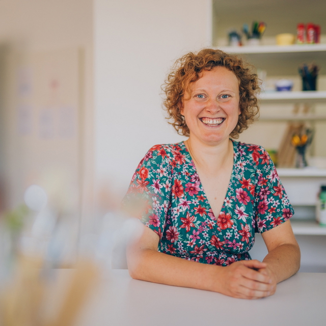 Kunsttherapeutin in einem farbenfrohen Kunstraum lächelt in die Kamera.