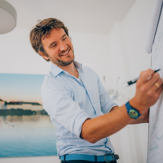Ein Mann in einem blauen Hemd schreibt etwas auf ein Flipchart.