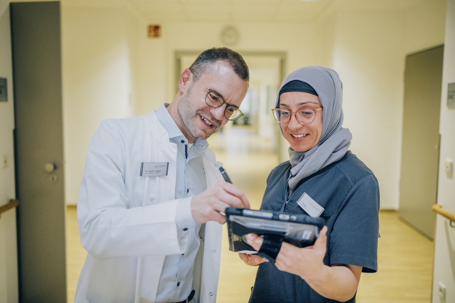 Ein Mann und eine Frau stehen in einem Klinikhausflur und sprechen miteinander.