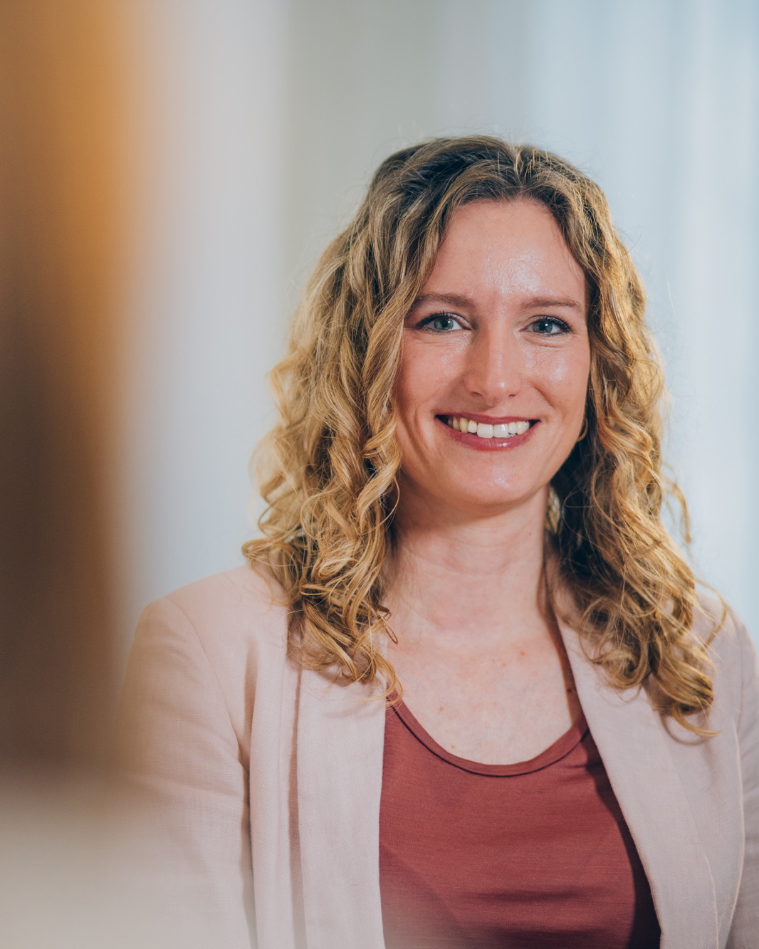Eine lächelnde Frau sitzt in einem Büro gegenüber einer anderen Frau und strahlt Freude und Zufriedenheit aus.