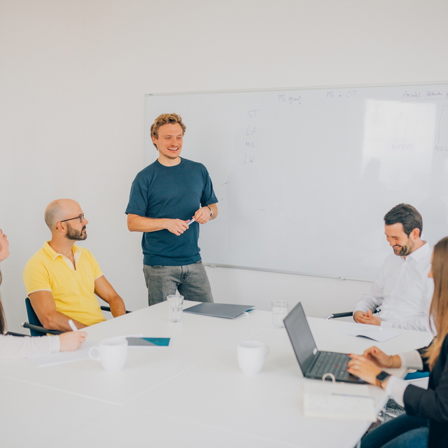 Fünf Personen sind um einen Tisch versammelt und besprechen sich.