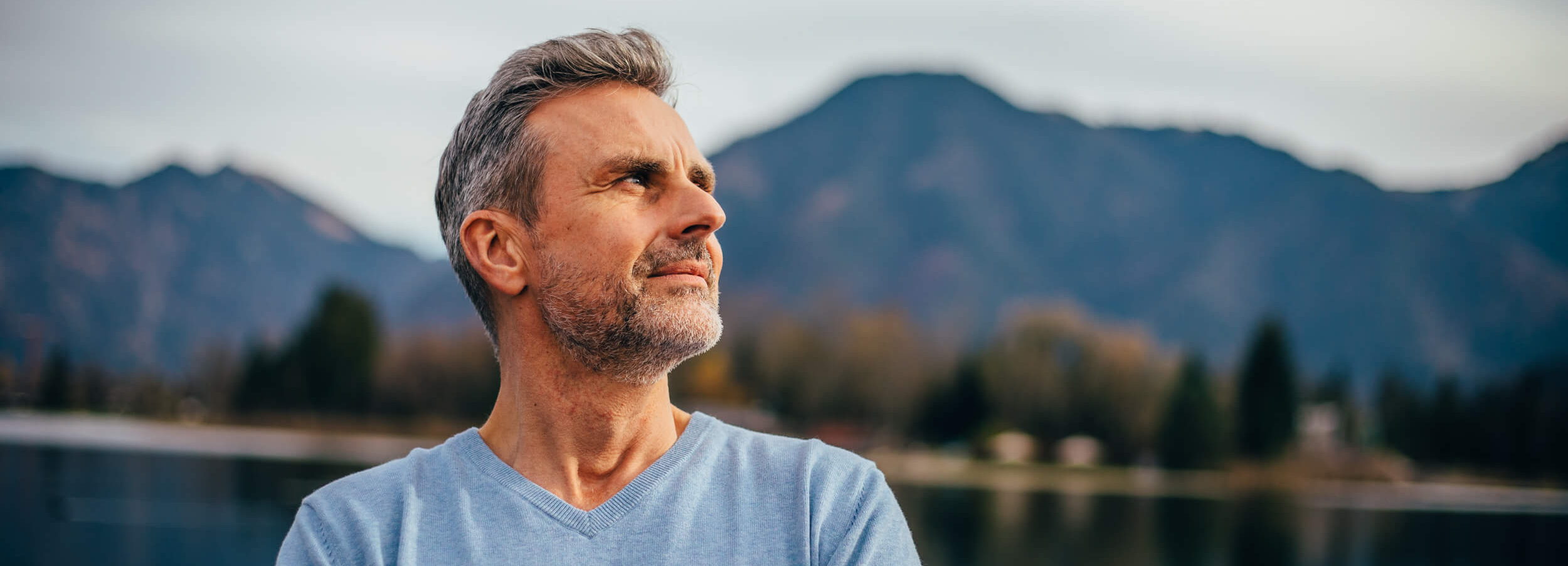 Mann schaut in die Ferne vor einer Gebirgskulisse mit See