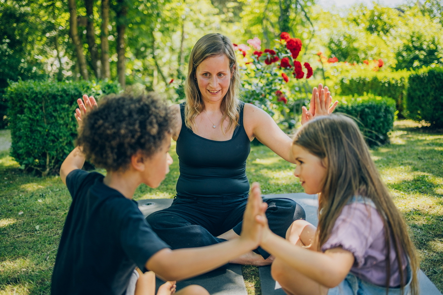 Sozialpädagogin beschäftigt sich im Garten mit zwei Kindern.
