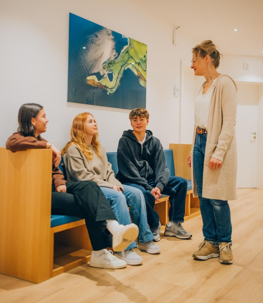 Eine Frau spricht mit einer Gruppe von Jugendlichen in einem Wartezimmer.