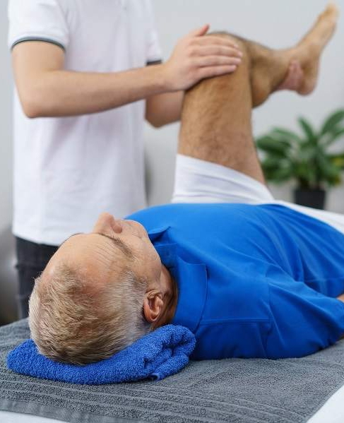 Ein Patient liegt auf dem Rücken und wird während der Orthopädie-Reha behandelt