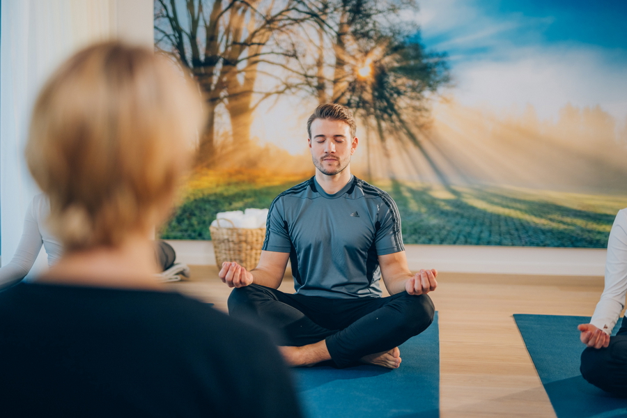 Ein Mann sitzt im Schneidersitz auf einer Matte während einer Meditation in der Reha Klinik.