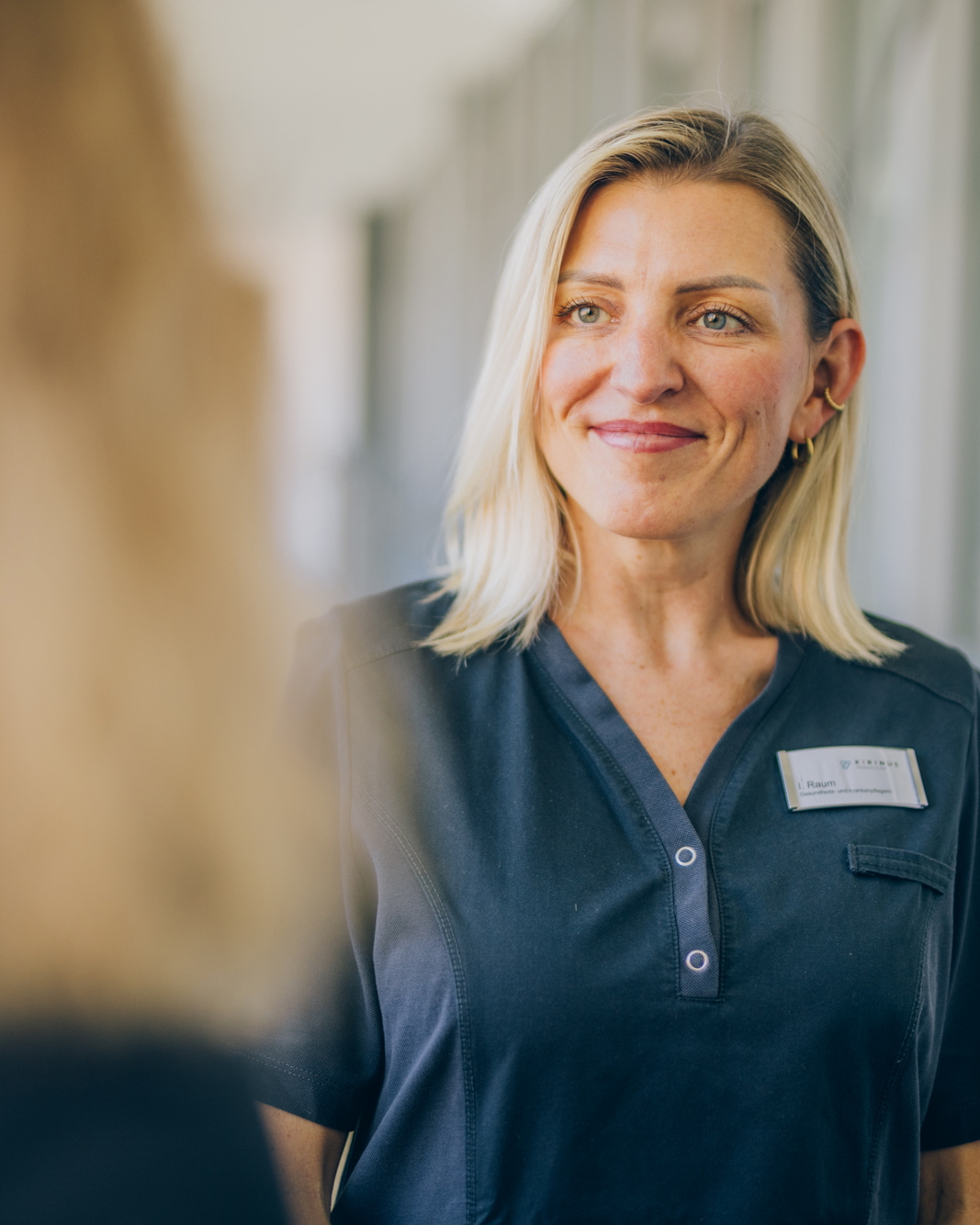 Pflegefachkraft im Gespräch mit einer Kollegin auf einem Klinikflur.