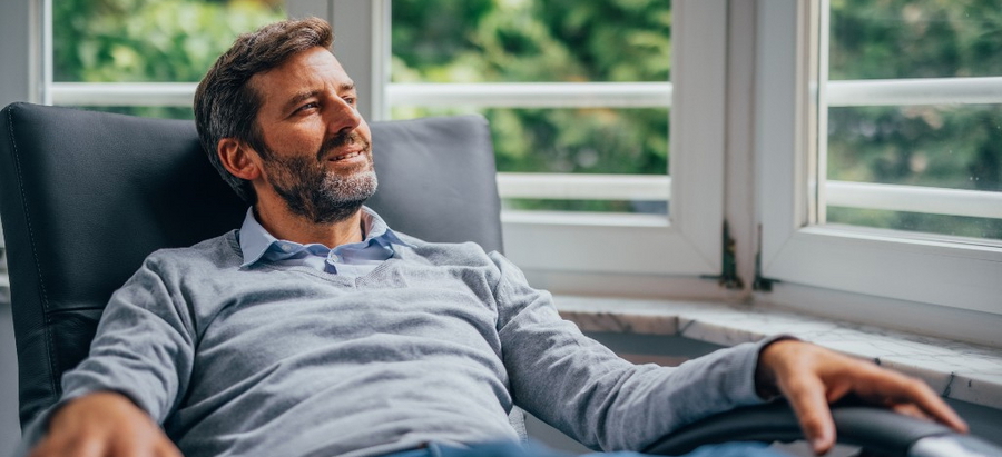 Mann sitzt im Sessel und sieht gedankenverloren aus dem Fenster
