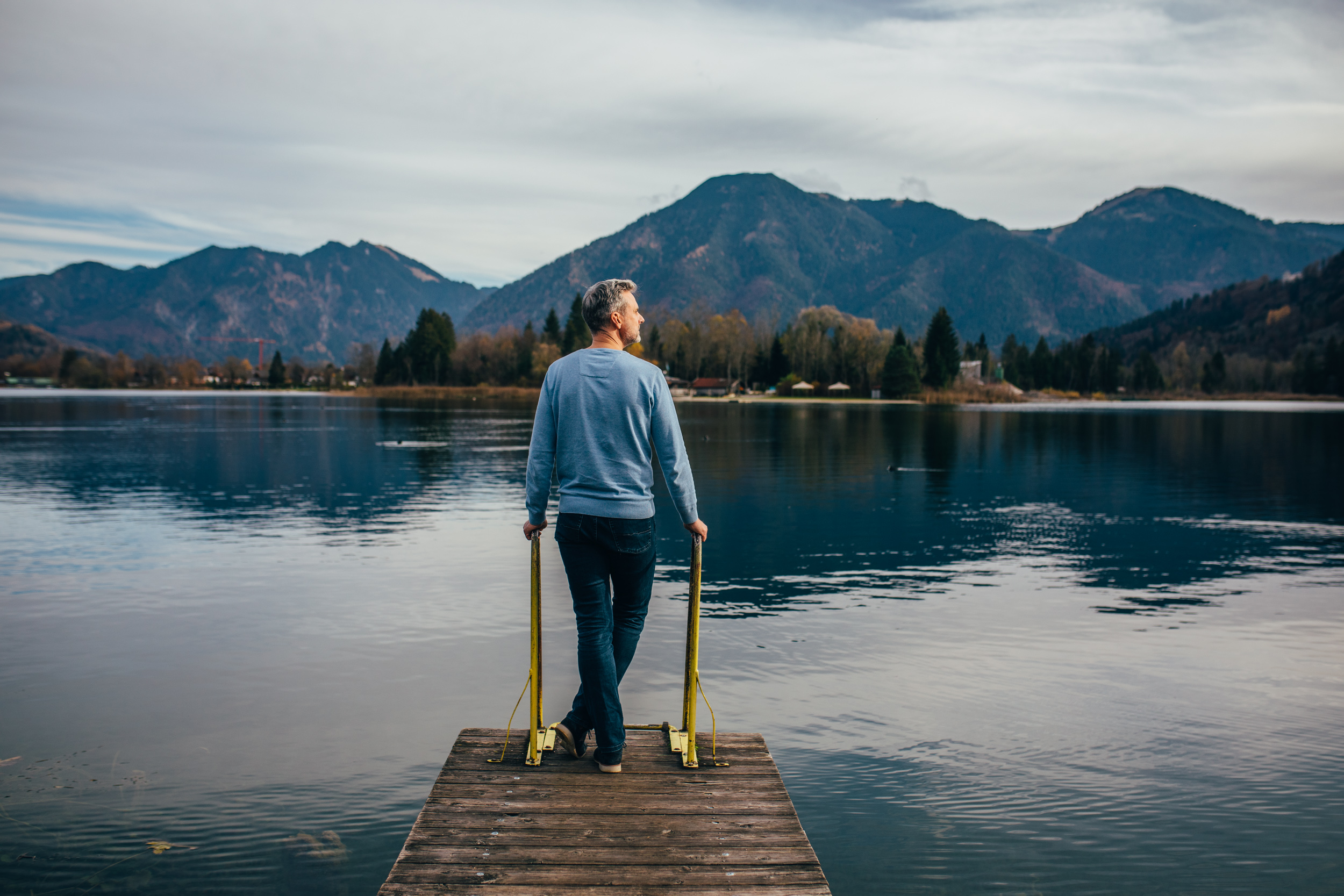 Ein Mann steht auf einem Steg am Tegernsee mit Bergpanorama im Hintergrund.