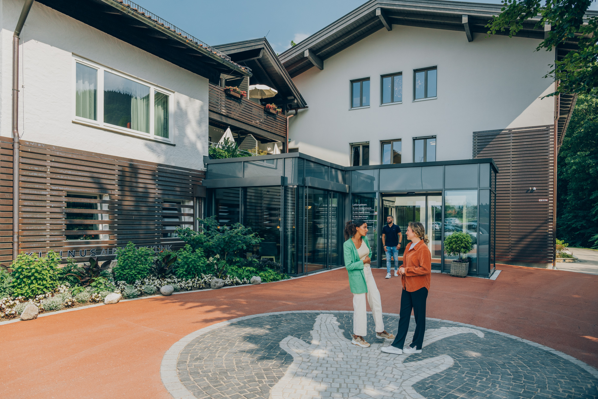 Zwei Frauen stehen vor der KIRINUS Alpenpark Klinik am Tegernsee und unterhalten sich.