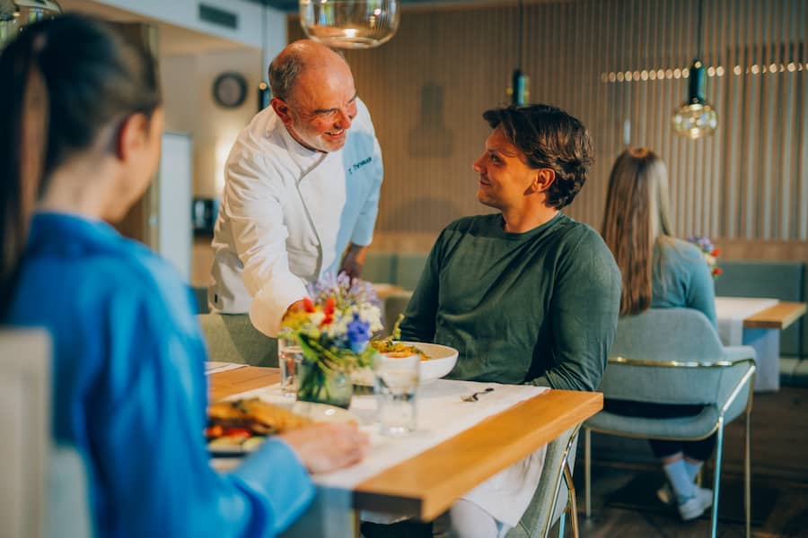 Küchenchef serviert seinen Gästen lächelnd einen Gruß aus der Küche.