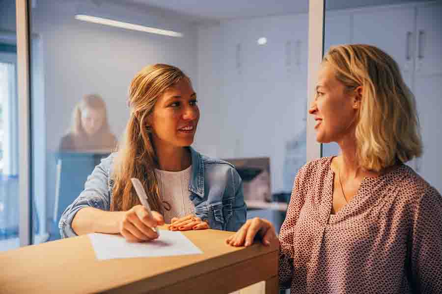 Zwei weibliche Personen unterhalten Sich am Empfangstresen bei KIRINUS