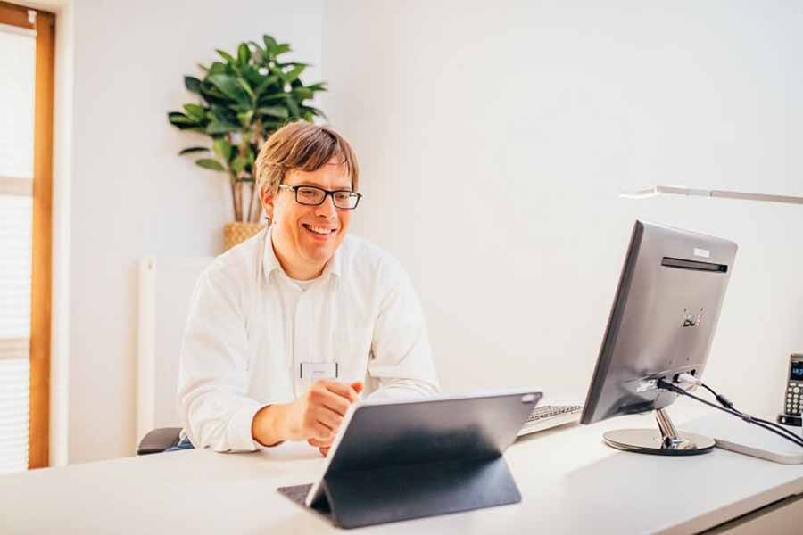 Neurologe sitzt im Behandlungszimmer am Schreibtisch vor seinem PC.