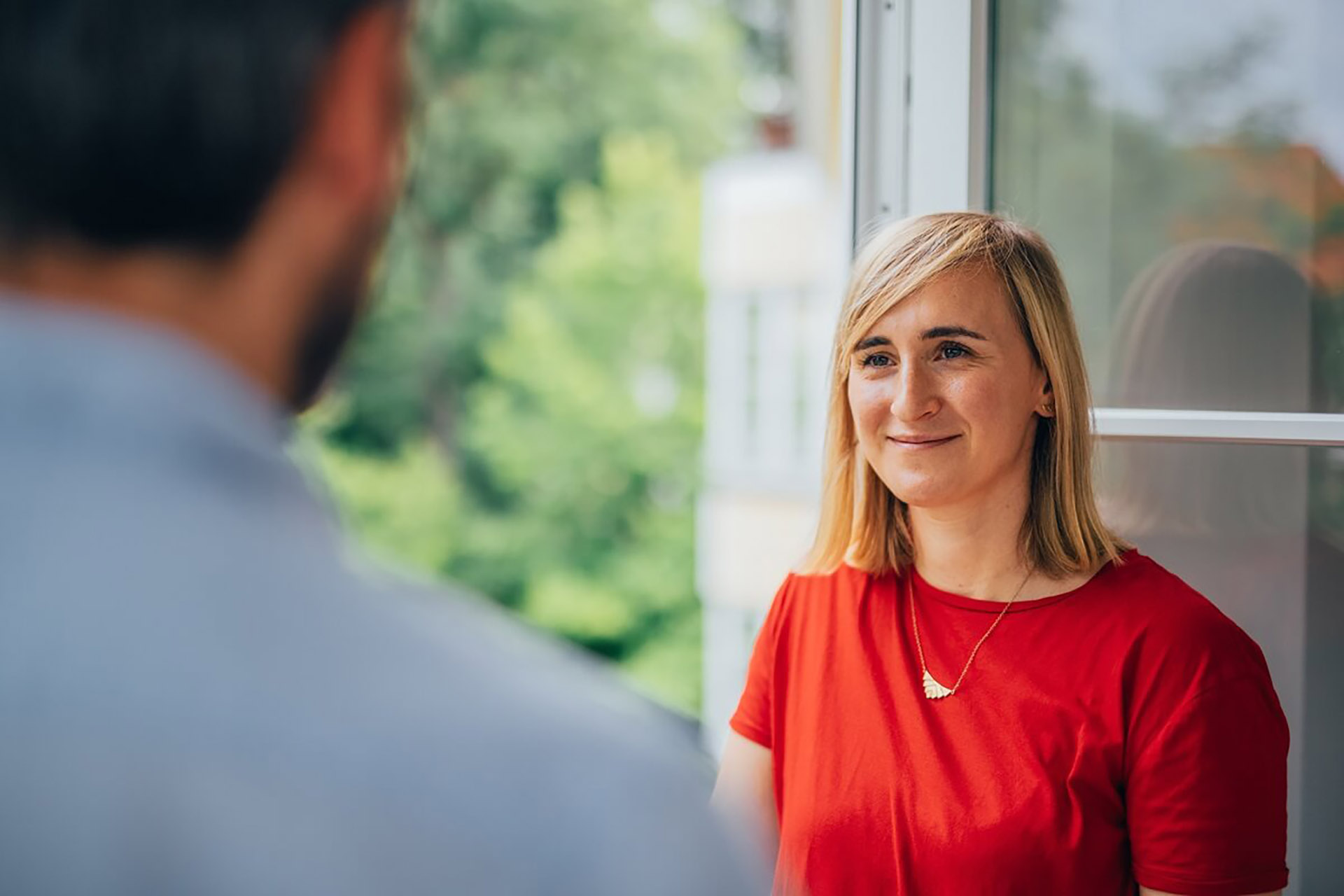 Gesprächssituation zwischen zwei Personen am Fenster mit Blick ins Grüne