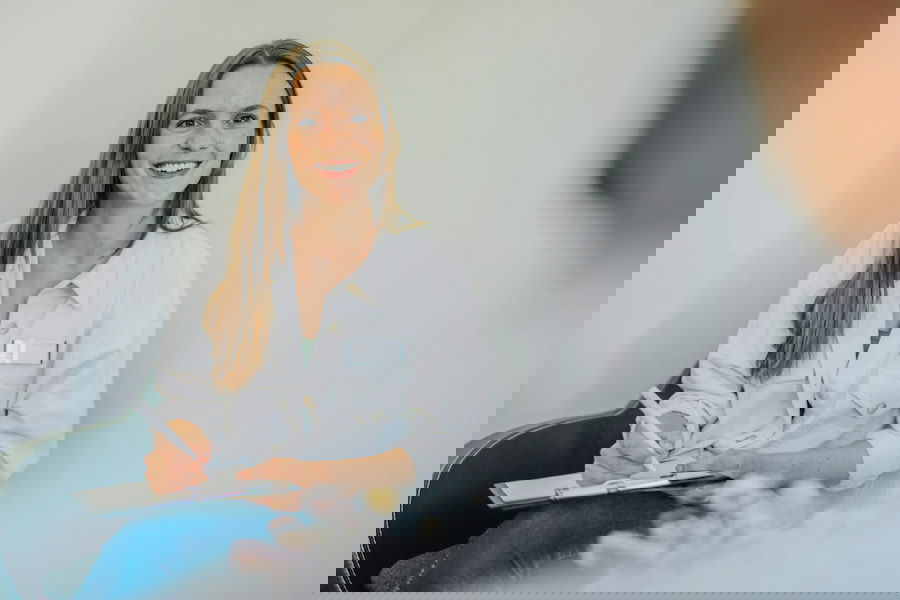 Eine Psychotherapeutin in Weiterbildung sitzt entspannt in einem Stuhl und notiert etwas mit einem Stift auf Papier.