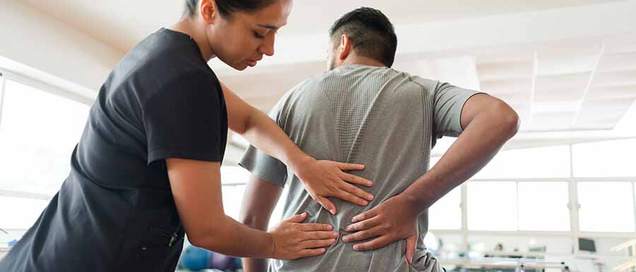 Physiotherapeutin tastet den Rücken eines Patienten ab während der Reha nach einem Bandscheibenvorfall