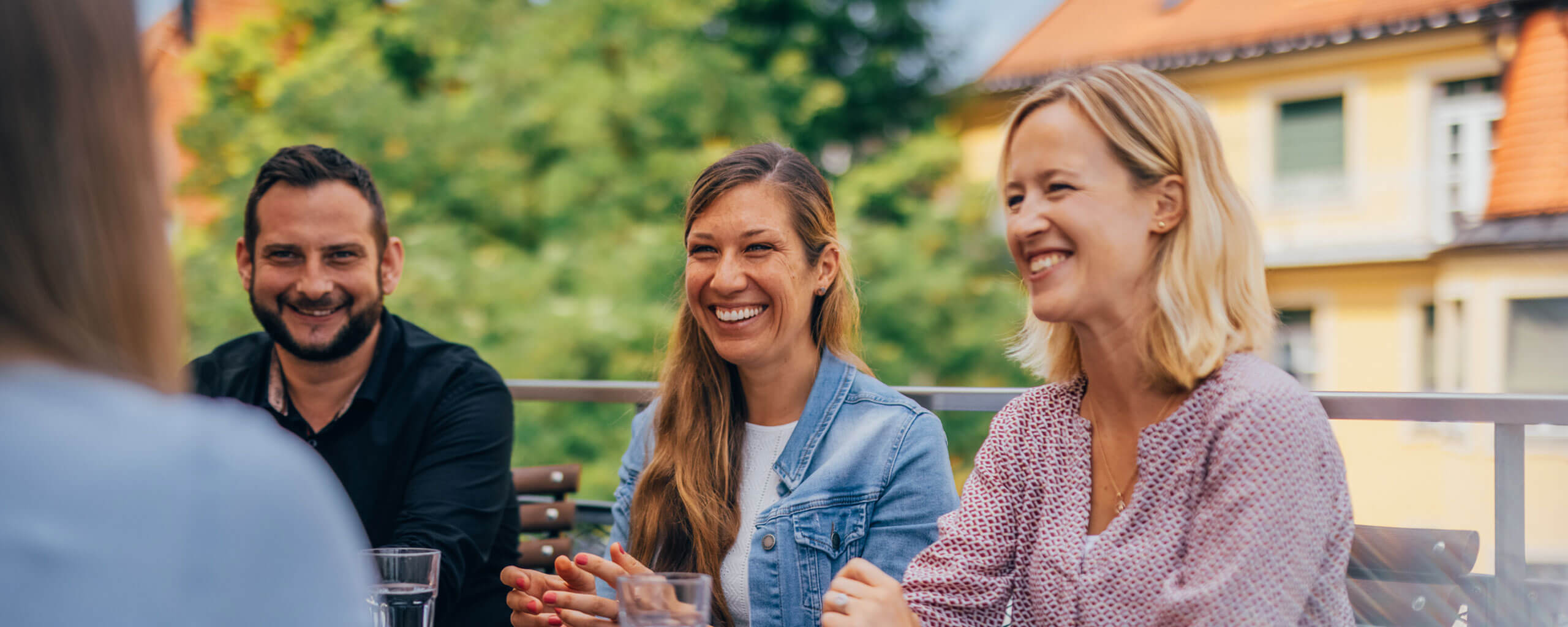 Mehrere Personen sitzen an einem Tisch auf der Sonnenterasse und Unterhalten sich